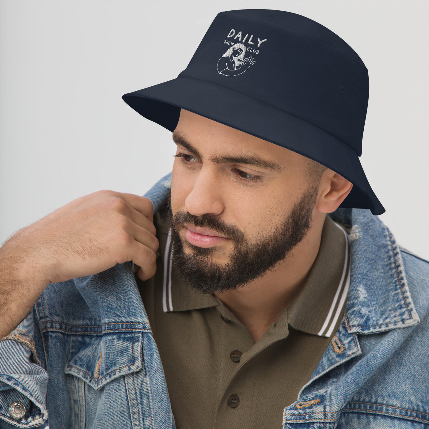 Man wearing a navy bucket hat with a logo, styled with a denim jacket, perfect for casual outings.