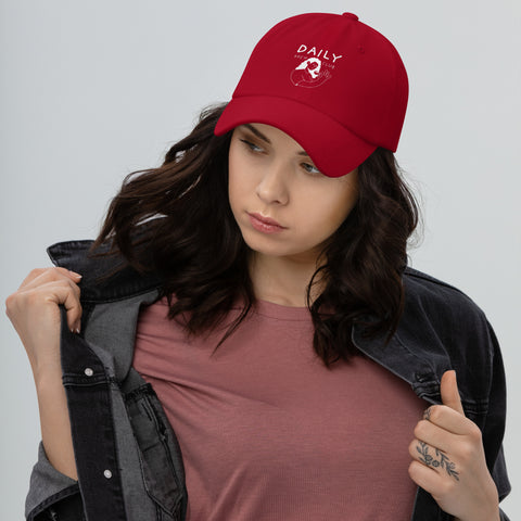 Red dad hat with 'DAILY' logo, worn by a young woman in a casual outfit, showcasing everyday style.
