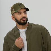 Man wearing a stylish olive green trucker cap with a mesh back and daily brand logo, paired with a bomber jacket.